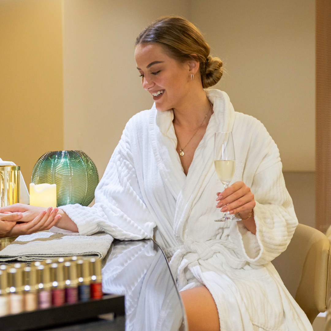 Woman in a white robe holding a glass of wine in a spa setting